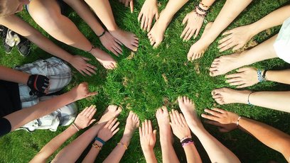 Viele Hände und Füße von verschiedenen Personen, die in einem Kreis auf einer grünen Wiese sitzen